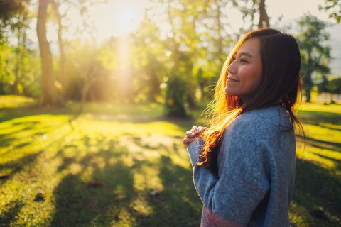 Selbstliebe: Frau steht glücklich im Park und genießt die Sonne