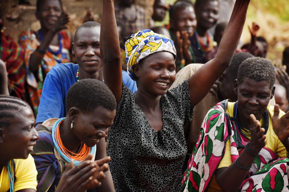 Frauen und Mädchen in Karamoja: Frau aus Karamoja schaut glücklich und hält die Arme in die Luft