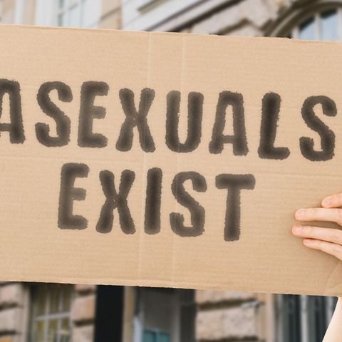 Asexualität: Hand hält ein Schild mit der Aufschrift "Asexuals Exist" ("Asexuelle existieren") in die Kamera