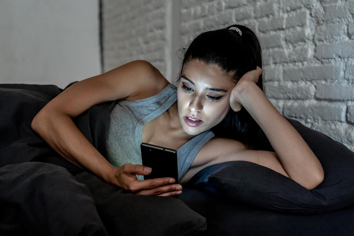 Kleine Häppchen online: Frau liegt in Bett und liest etwas auf ihrem Handy