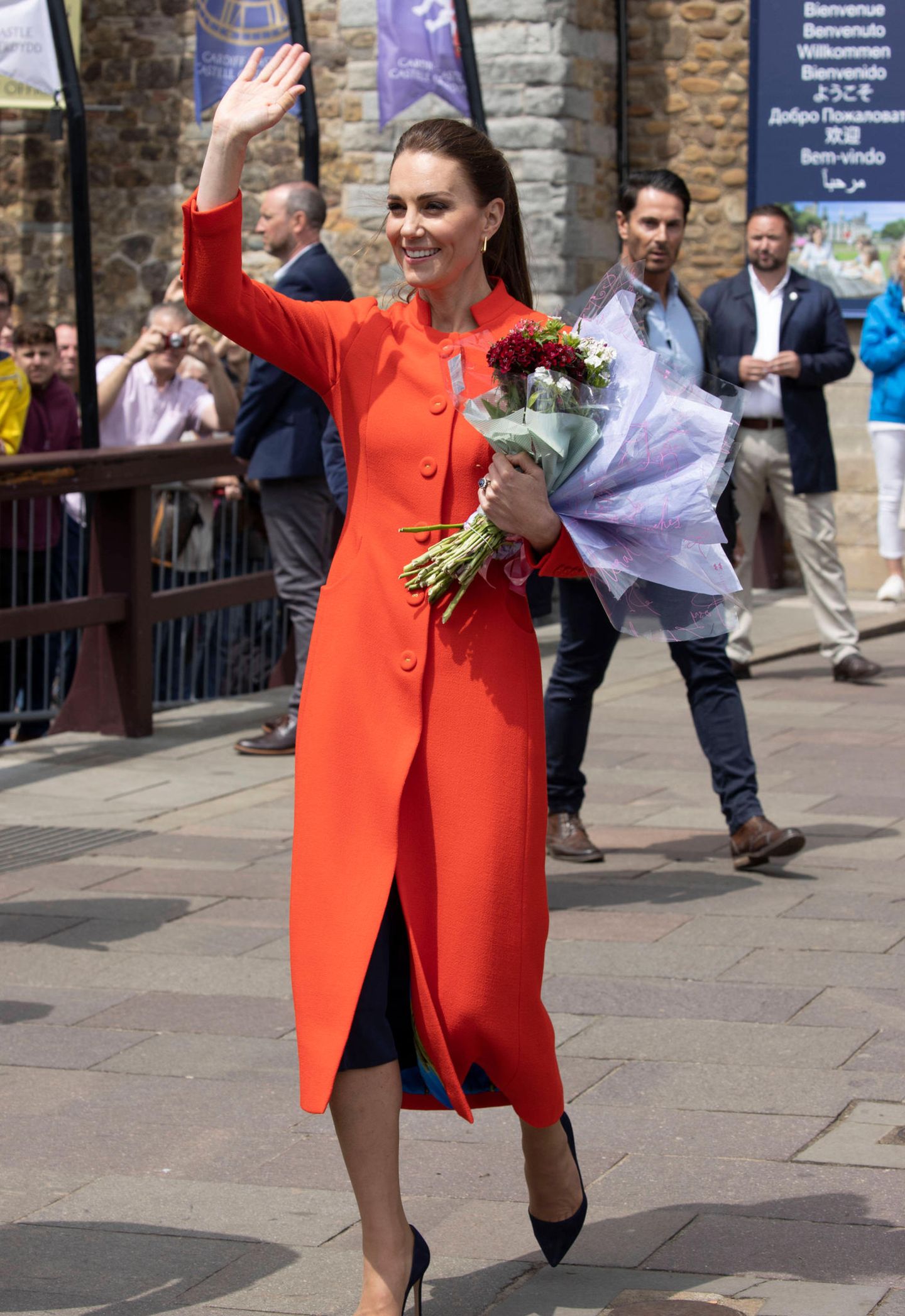 Beim Besuch des Cardiff Castle in Wales setzt die Herzogin von Cambridge auf einen Mantel in Rot-Orange überm schwarzen Kleid sowie ein strahlendes Lächeln. Ihre Haare trägt Catherine zu einem entspannten Pferdeschwanz, Schmuck und Schuhe bleiben mit kleinen goldenen Creolen und schwarzen Pumps ebenfalls klassisch und dezent. 