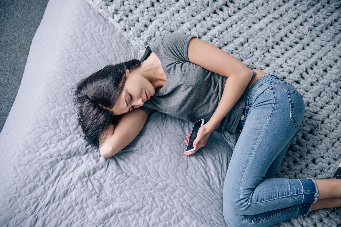 Frau auf dem Bett, traurig mit Smartphone