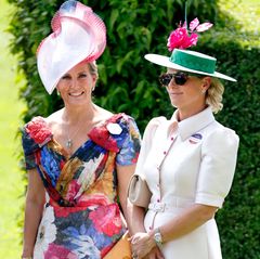 Gräfin Sophie lässt sich von dem bunten Treiben in Ascot inspirieren und wählt am Ladys Day ein florales Kleid mit V-Ausschnitt von Suzannah. Dazu kombiniert sie einen Statement-Hut mit pinkfarbener Borte – ein ungewöhnlich extrovertierter Look für Sophie. 