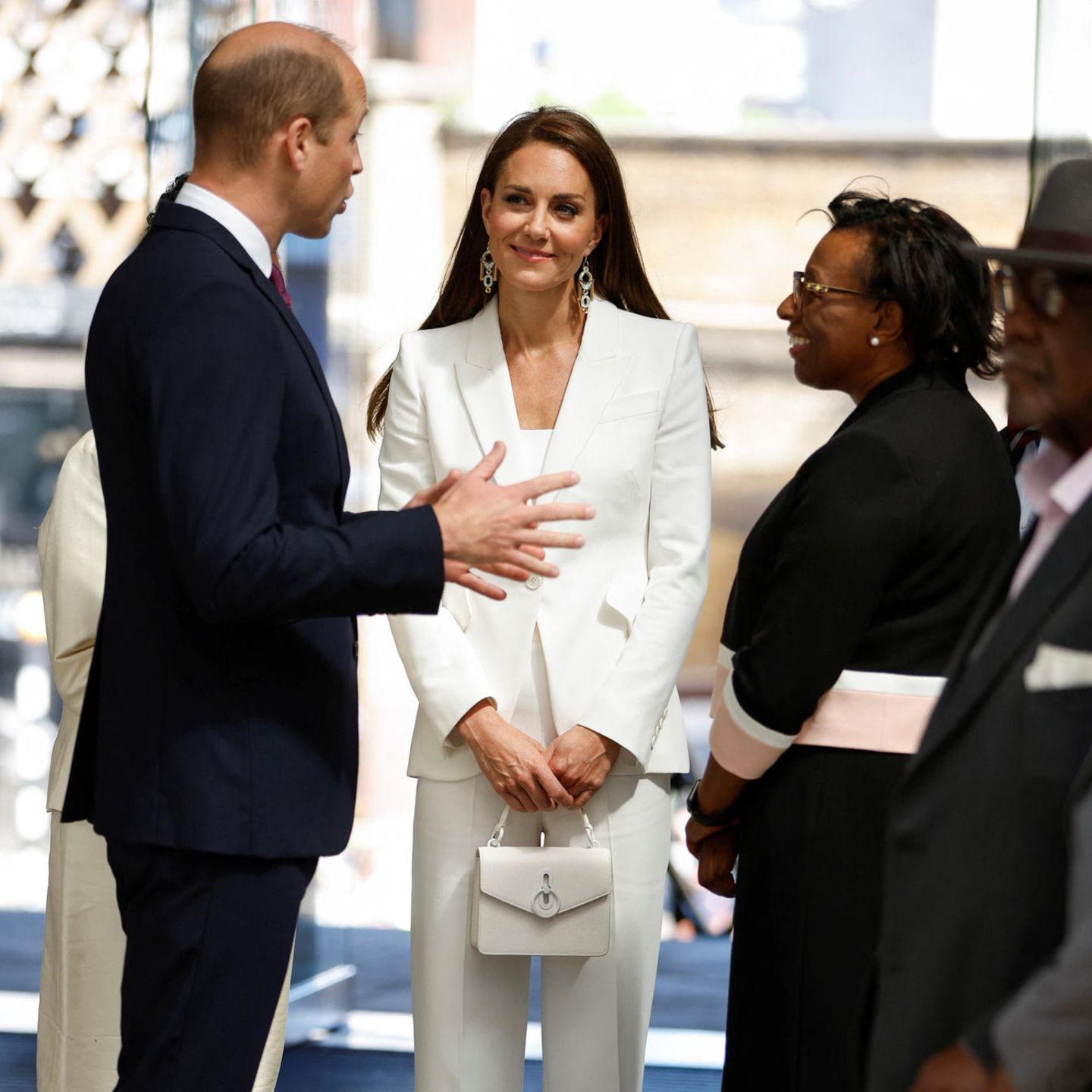 Die Haare trägt Herzogin Catherine ungewohnt glatt und im Seitenscheitel. Besonders auffällig sind auch Kates goldfarbene Glamour-Ohrringe, die mit Perlmutt-Elementen das Weiß des Anzugs wieder aufgreifen. 