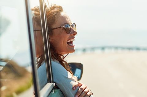 Weltreise durch Deutschland: Frau schaut lachend aus dem Autofenster