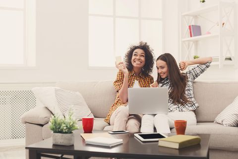 zwei junge Frauen sitzen auf deinem Sofa beim Online SHopping