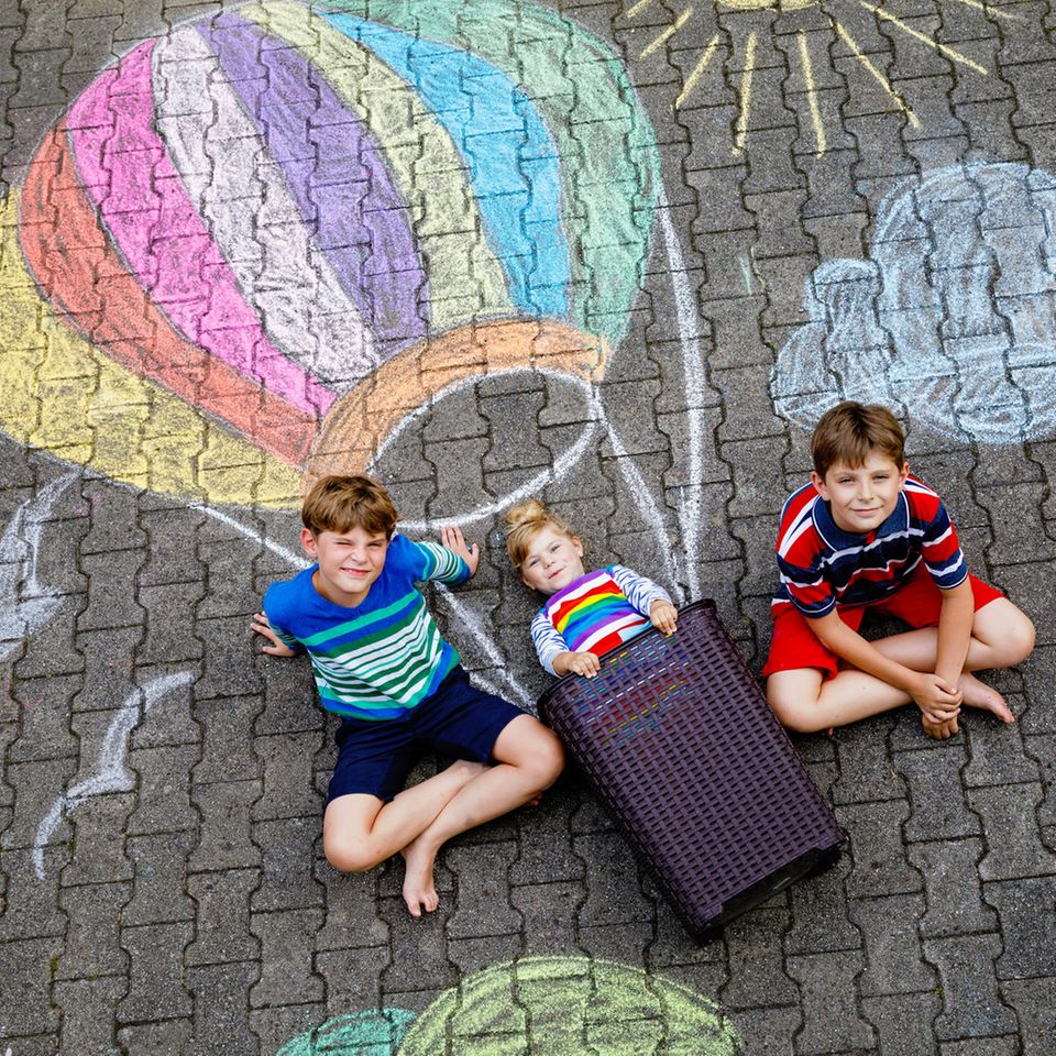 Charakterstärke: Drei Kinder sitzen zufrieden vor ihrer Kreidemalerei