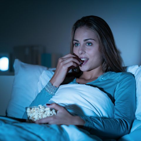 TV-Lieblinge: Frau guckt einen Film im Bett und isst dabei Popcorn.