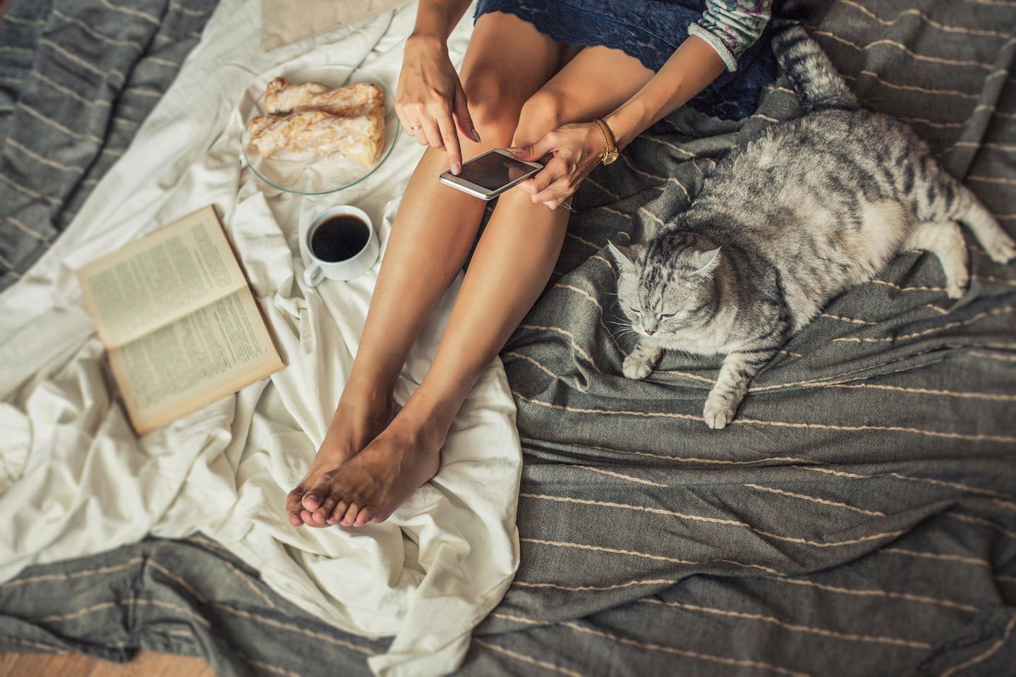 Frau mit Buch und Smartphone: 7 Bookstagram-Trendbücher, die den Hype absolut wert sind
