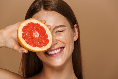 junge Frau mit Sommersprossen und einer Grapefruit vor dem Gesicht