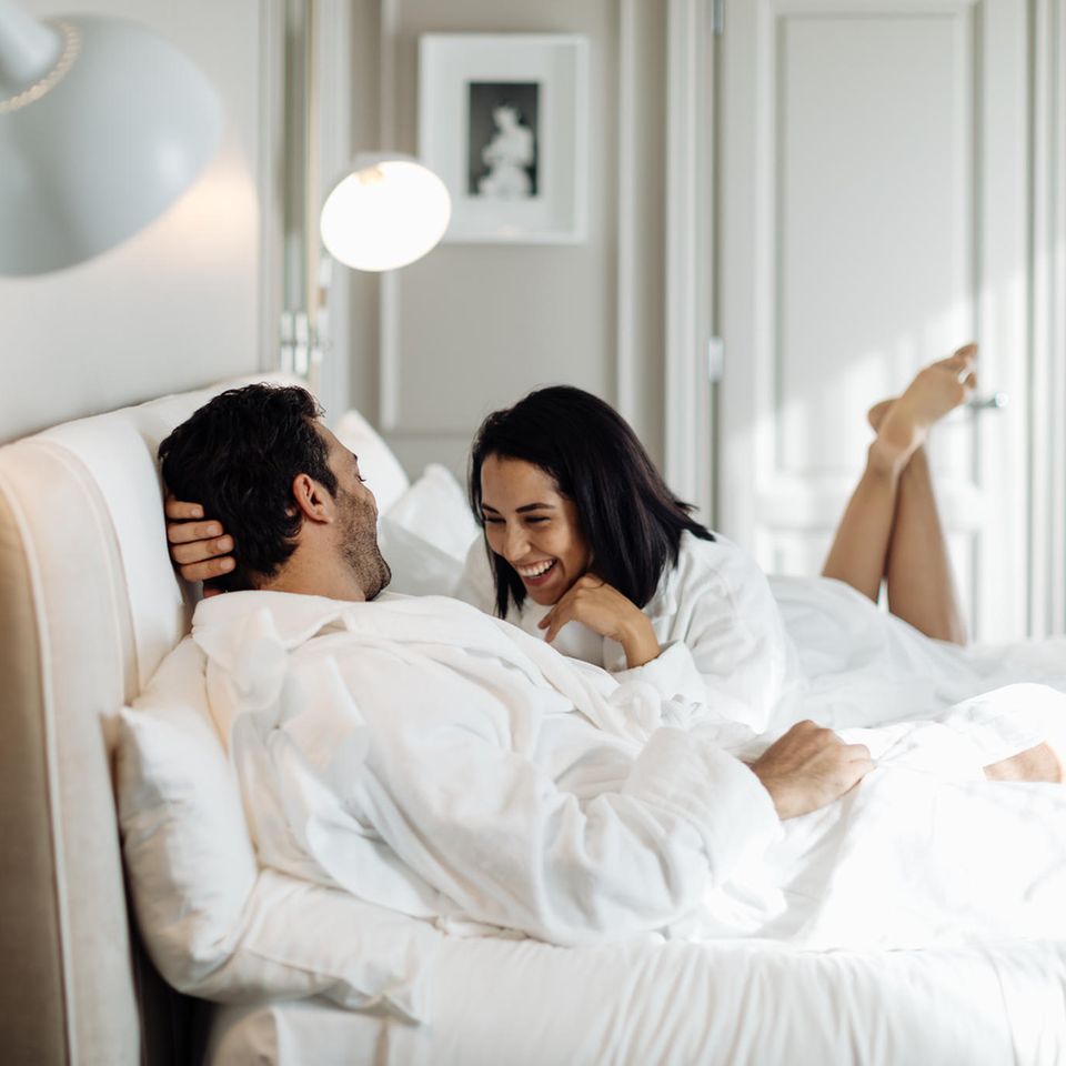 Ein Mann und eine Frau liegen im Bett und lachen.