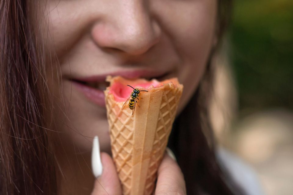 Eine Frau isst ein Eis, auf deren Waffel eine Wespe sitzt