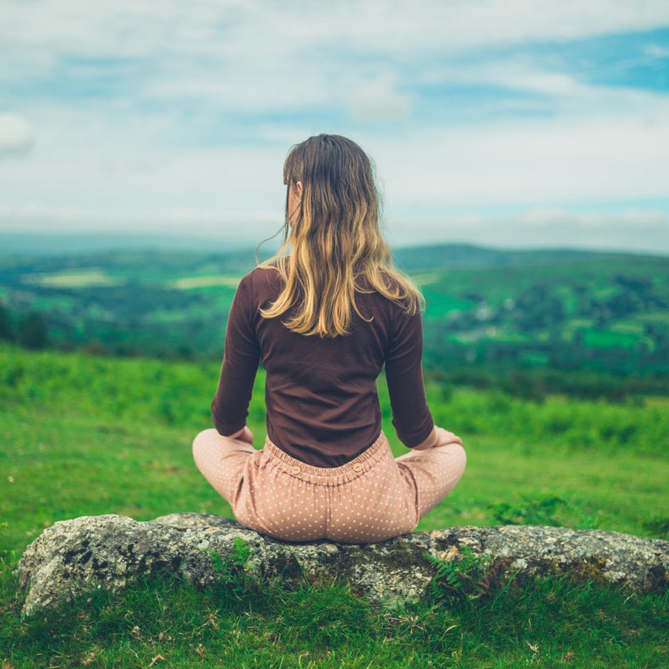 Frau sitzt auf Fels in der Natur | Die Stein-Strategie: Wie du mit Nichtstun glücklicher und erfolgreicher wirst