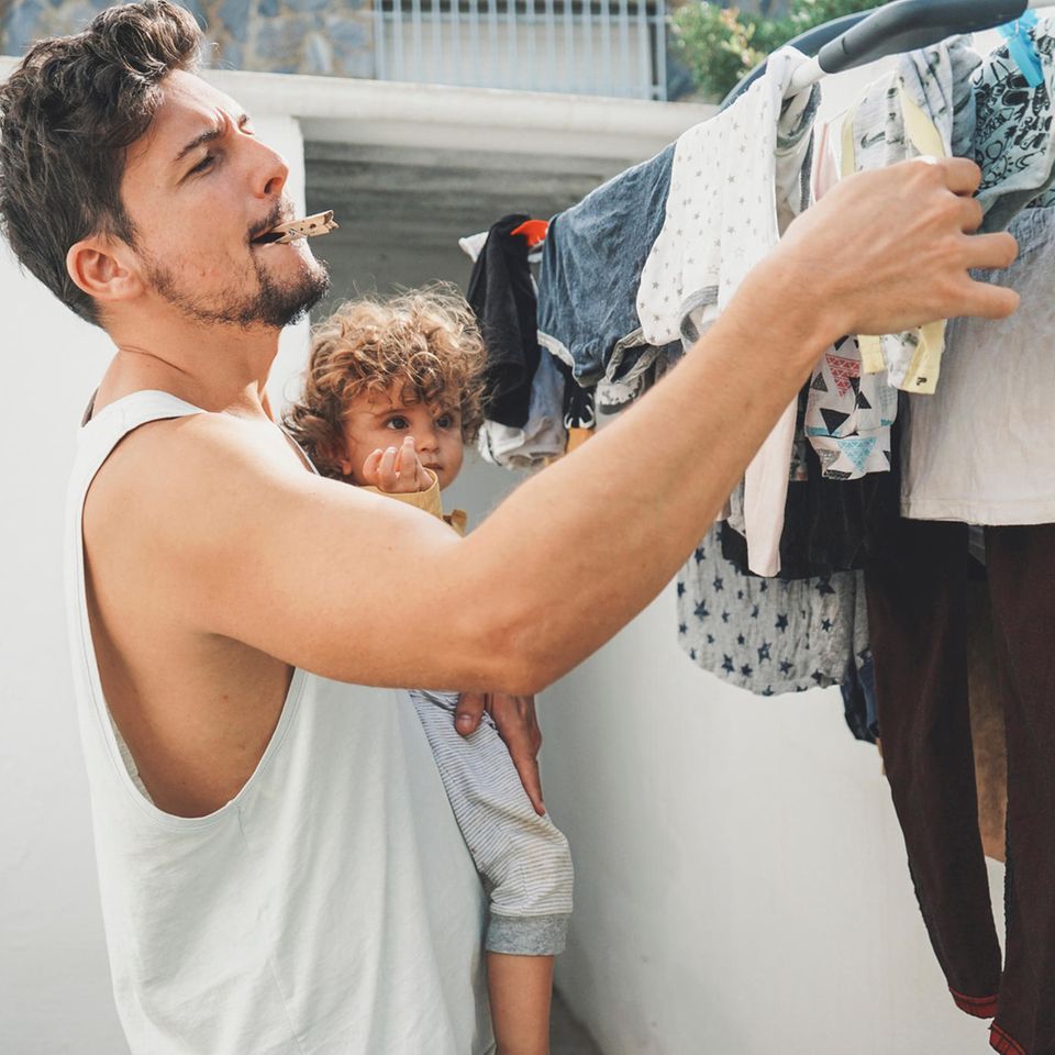 Umweltbewusst von Anfang an: Vater mit Kind auf dem Arm hängt die Wäsche auf