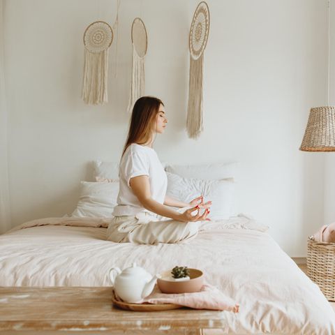 Frau sitzt auf einem Bett und meditiert