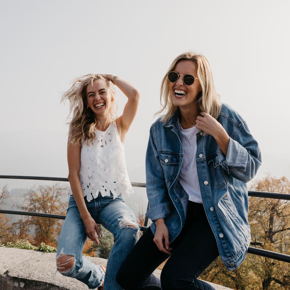 Zwei Frauen sitzen auf einem Geländer und lachen.