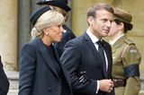 Die Frau des französischen Präsidenten, Brigitte Macron, ehrt Queen Elizabeth, indem sie sich streng an den Dresscode hält: Sie trägt zum schwarzen Kleid mit Mantel eine schwarze Strumpfhose, Lederhandschuhe und einen Hut mit Netzschleier. 