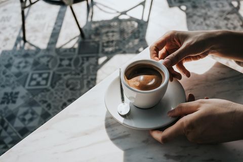 Eine Frau stellt eine Tasse Kaffee auf einem Tisch ab.
