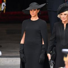 Zum Begräbnis der Queen zeigt sich Herzogin Meghan in einem recht schlichten Look, der jedoch mehr Geschichte hat, als gedacht. Sie trägt ein Cape-Dress von Stella McCartney in Midilänge, dazu eine schwarze Strumpfhose, die Perlenohrringe, die sie von der Queen geschenkt bekommen hat sowie einen schwarzen Hut von Dior. Aufmerksamen Beobachter:innen mag aufgefallen sein, dass Meghan das gleiche Kleid schon einmal getragen hat ... 