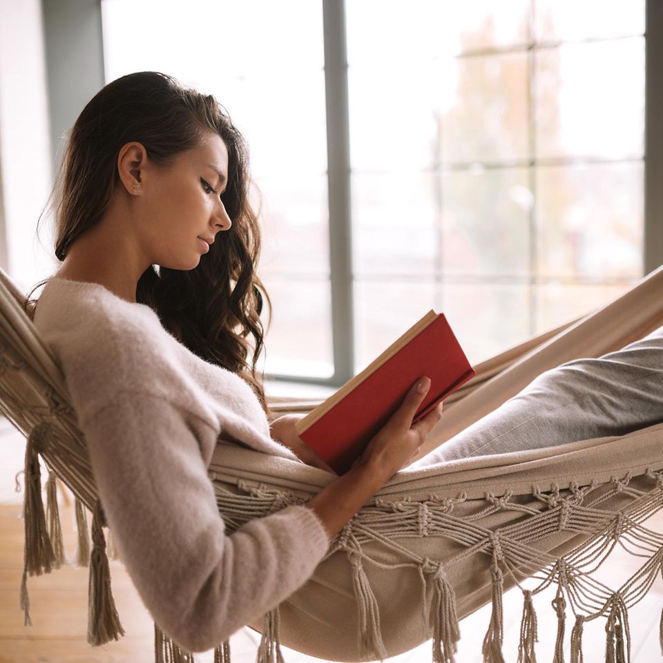 Junge Frau liegt in einer Hängematte und liest dabei ein Buch