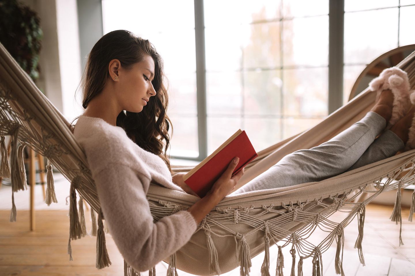 Junge Frau liegt in einer Hängematte und liest dabei ein Buch