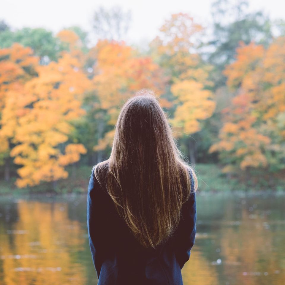 Frau schaut auf See mit Bäumen: 7 Warnsignale, dass du zu selbstkritisch bist