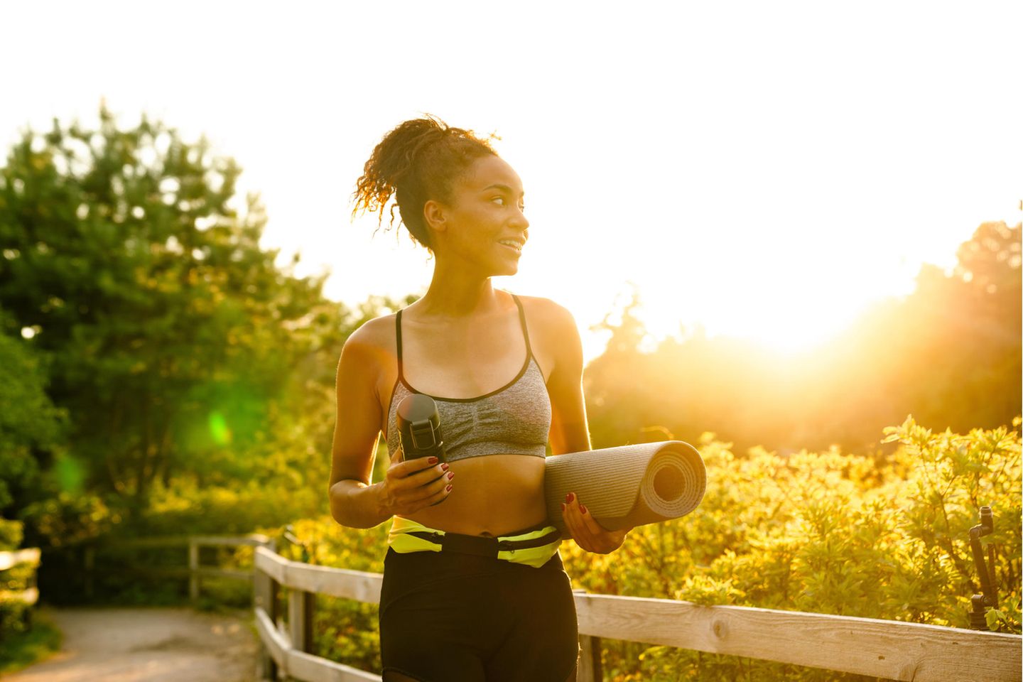 Frau mit Yogamatte im Park: Um diese Uhrzeit solltest du am besten Sport machen