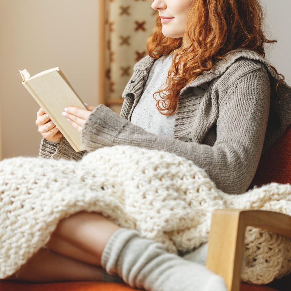 Frau liest im Sessel ein Buch: 4 romantische Bücher, die uns graue Herbsttage versüßen