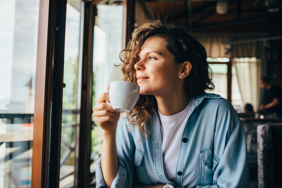 Eine Frau trinkt zufrieden eine Tasse Tee und schaut aus dem Fenster