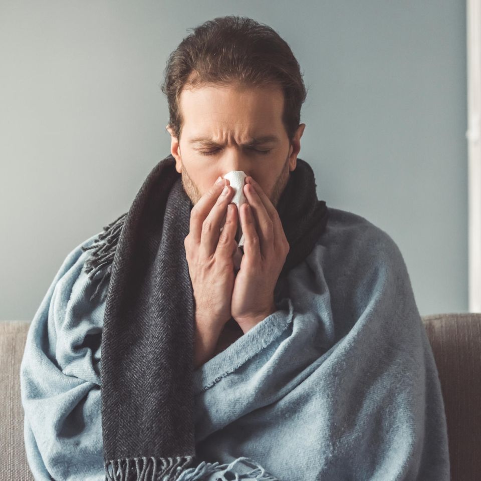Grippe oder Erkältung: Kranker Mann putzt sich die Nase