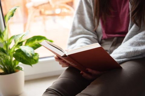 Buchtrends Herbst 2022: Frau sitzt auf Fensterbank und liest
