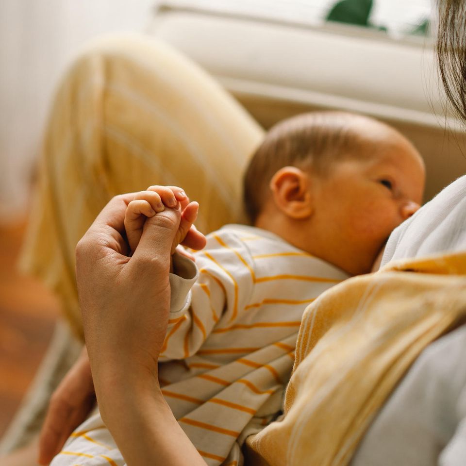 Eine stillende Frau hält währenddessen die Hand ihres Babys