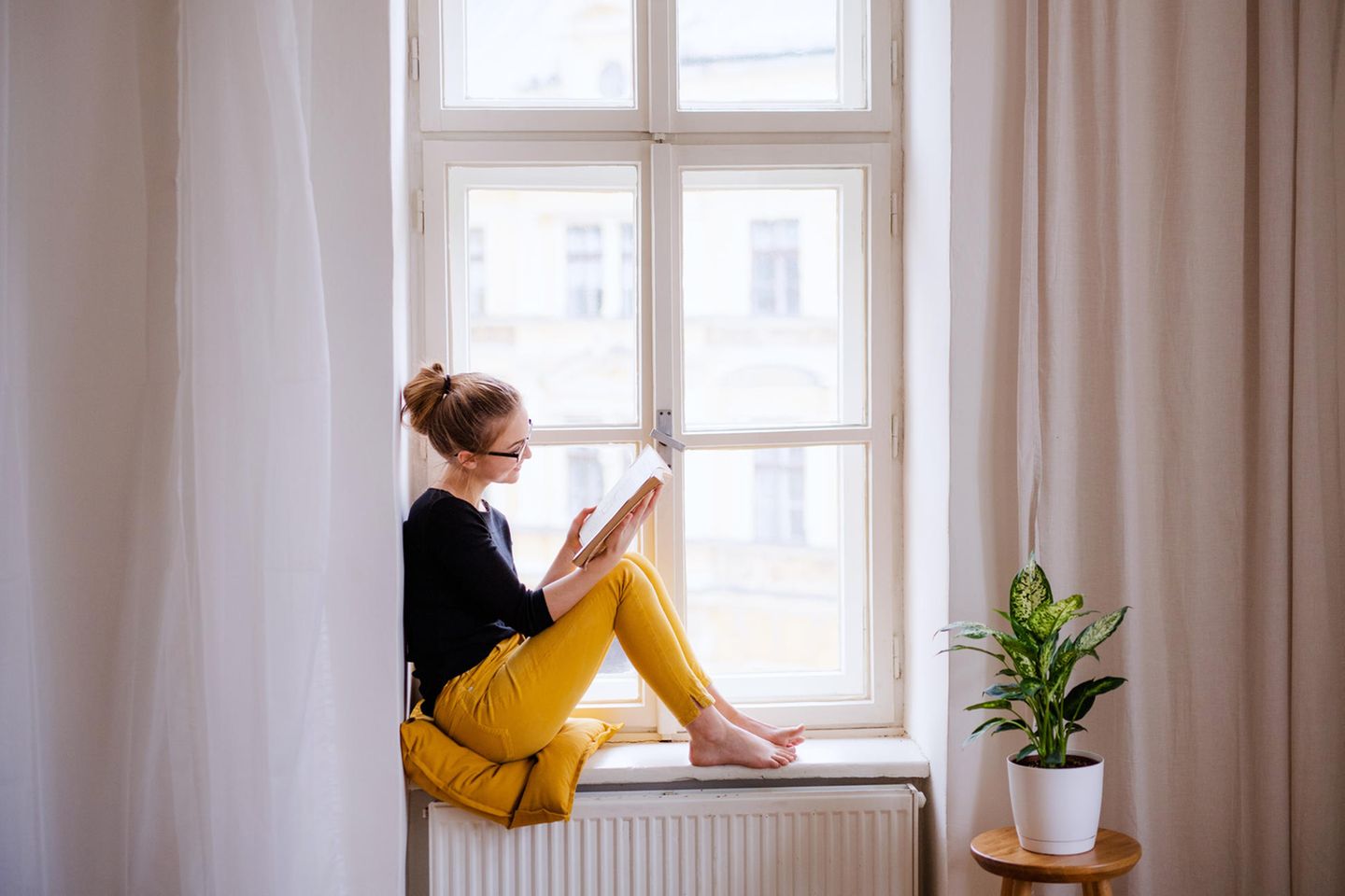 Frau liest ein Buch vor dem Fenster: Diese 5 Erfolgs-Serien beruhen auf richtig guten Büchern