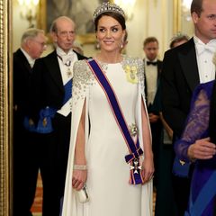 Beim ersten Staatsbankett während der Regentschaft von König Charles III. ist Catherine, Princess of Wales, der Hingucker des Abends. Die Wahl ihres Kleides und des Schmucks sind dabei besonders spannend. Denn, ihre bezaubernde Traumrobe in Weiß ist eigentlich ein Brautkleid. Es hat jedoch einen besonderen Kniff: An dem Kleid ihrer Lieblingsdesignerin Jenny Packham stechen besonders die aufwendige Schulterpartie mit Pailletten in Blumenform und die Cape-Ärmel hervor. Dazu wählt die Princess of Wales einen hochkarätigen Kopfschmuck: Die "Cambridge Lover's Knot" Tiara, welche ein Hochzeitsgeschenk für Prinzessin Diana war. Ihr luxuriöses Auftreten wird durch ein Armband von Queen Elizabeth II. ergänzt. 