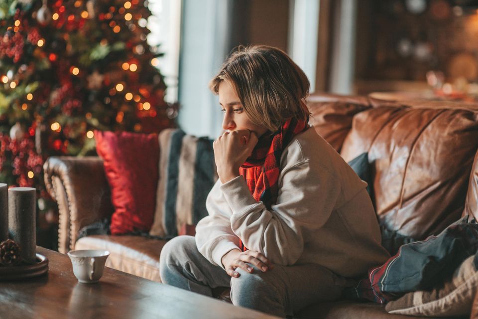 Eine Frau sitzt frustriert vor einem Weihnachtsbaum auf ihrem Sofa