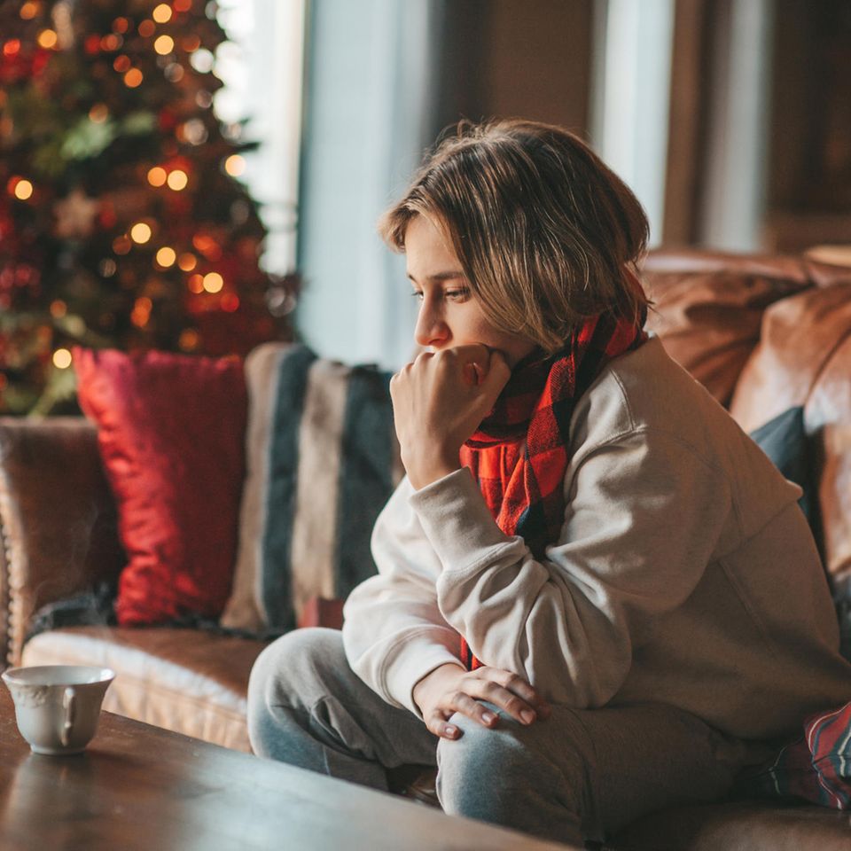 Eine Frau sitzt frustriert vor einem Weihnachtsbaum auf ihrem Sofa