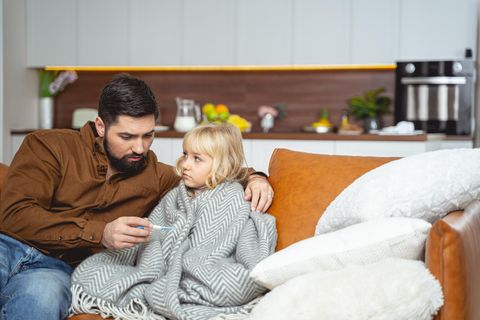 Ein Vater sitzt mit seiner kranken Tochter auf der Couch