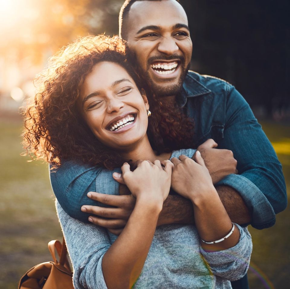 Ein Mann und eine Frau umarmen sich lachend in einem Park