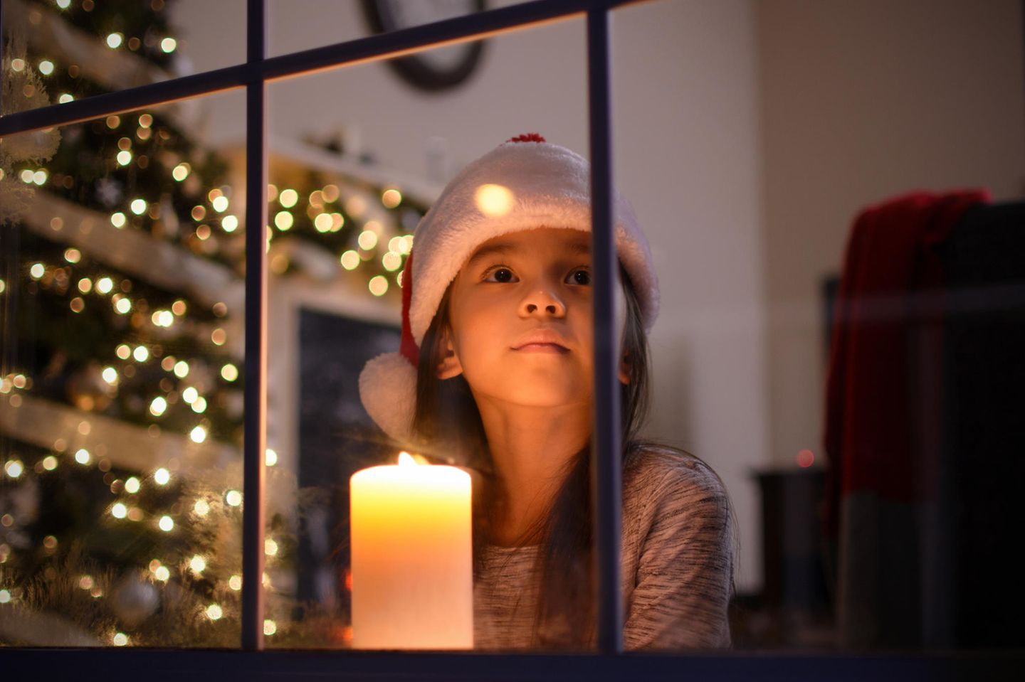 Mädchen mit Weihnachtsmütze und Kerze am Fenster