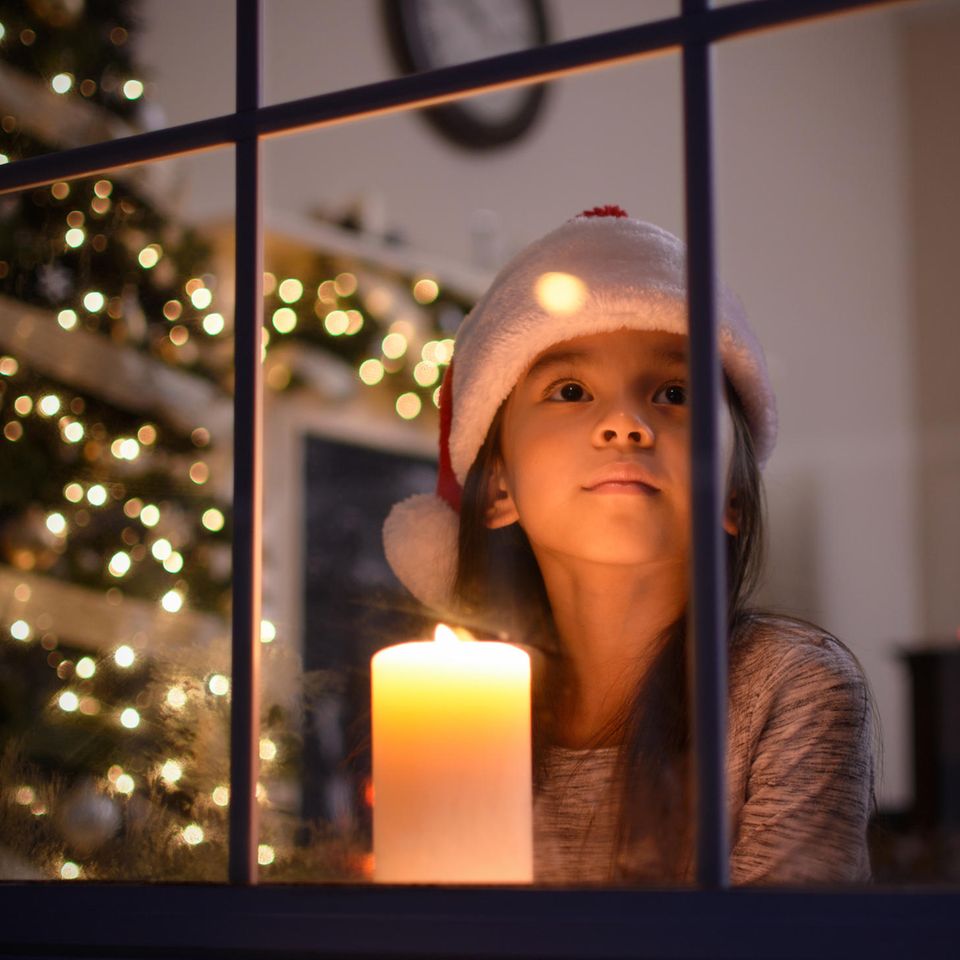 Mädchen mit Weihnachtsmütze und Kerze am Fenster