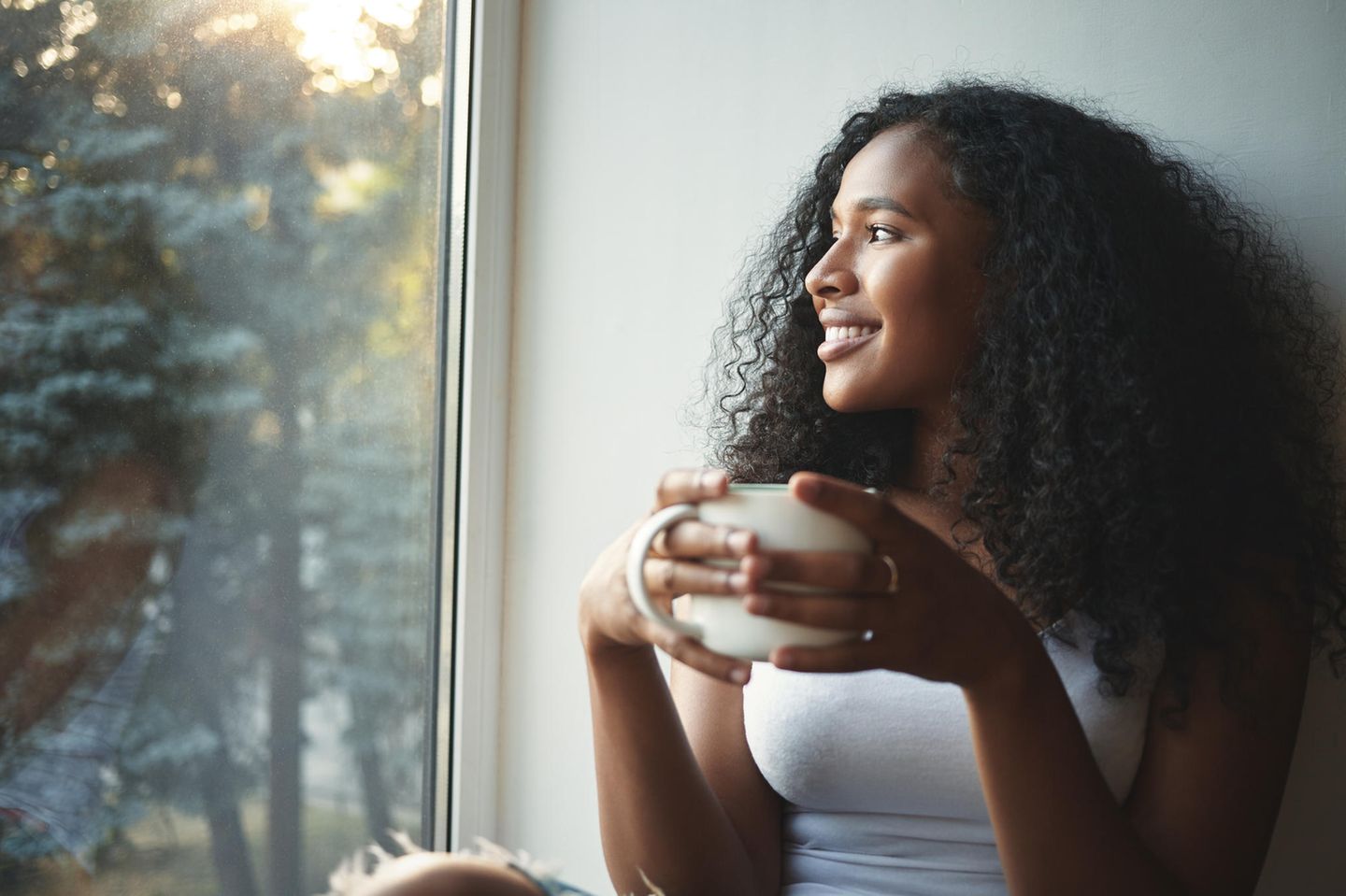 young woman sits with a cup of coffee at the window
