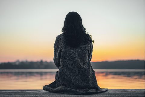 Frau schaut auf Sonnenuntergang über dem See: 5 Gründe, warum du nicht so glücklich bist, wie du sein solltest