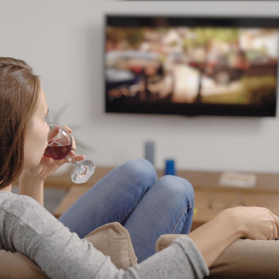 Frau mit Wein vor dem Fernseher: Diese Alltagsfehler sorgen klammheimlich dafür, dass du zunimmst