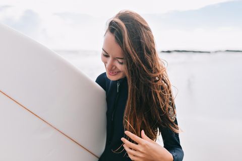 glückliche junge Frau mit Surfbrett unter dem Arm