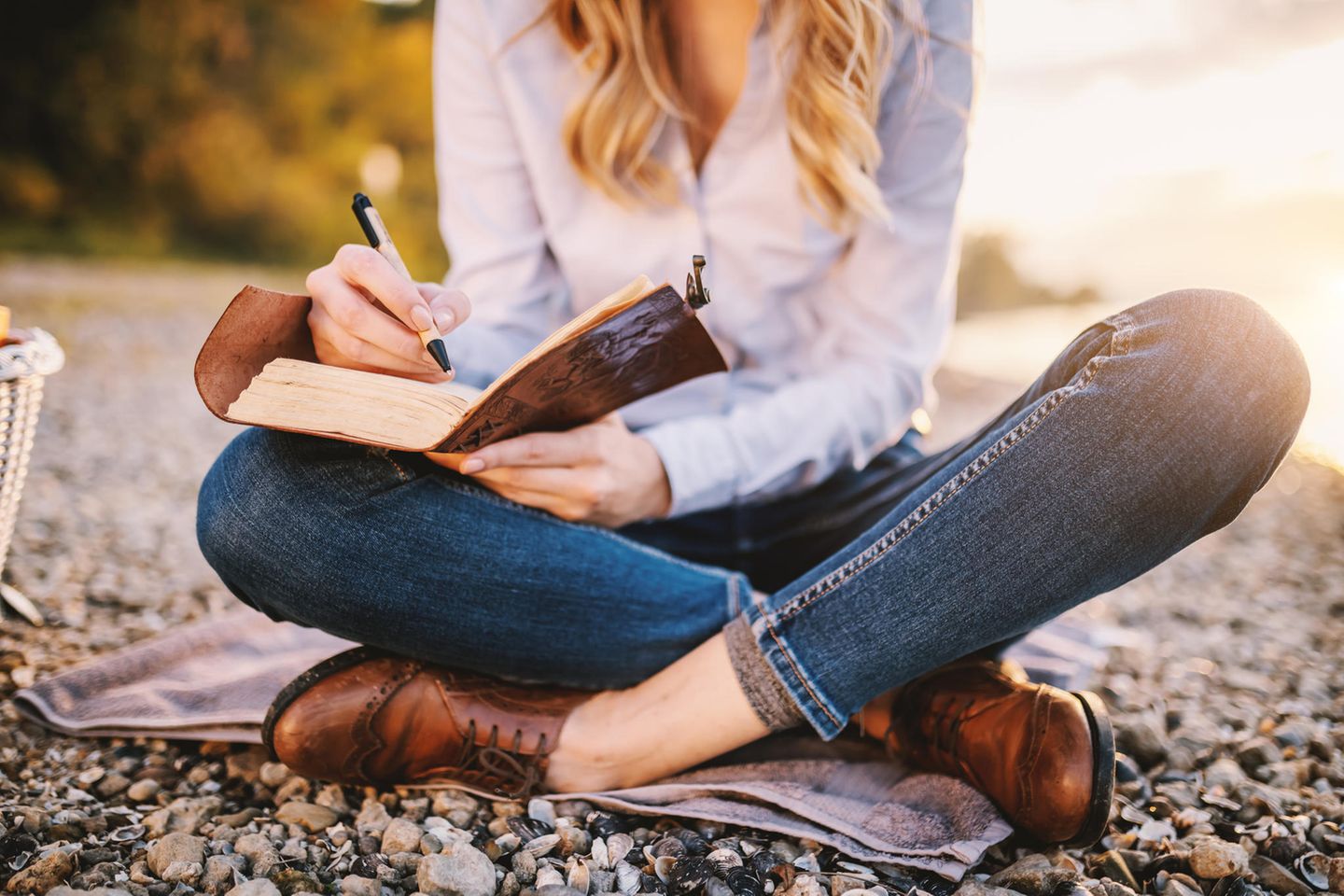 Eine Frau sitzt am Strand und schreibt in einem Buch