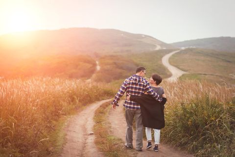 Verliebt in die beste Freundin: Ein Paar geht Arm in Arm einen Feldweg entlang