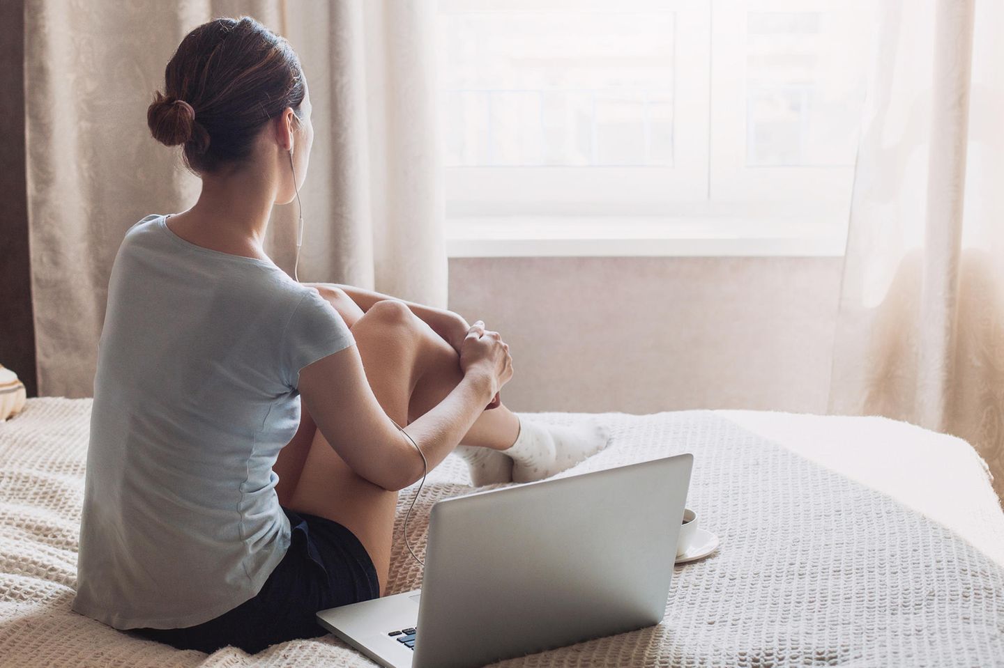Deepfake-Pornos: Eine junge Frau sitzt neben ihrem Laptop auf dem Bett