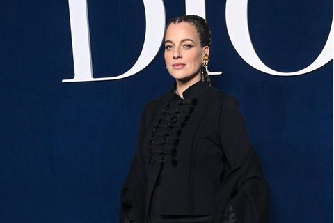 Cleo zu Oettingen-Spielberg trägt für die Dior-Show in Paris einen Look in Schwarz, die Jacke im Military-Style ist leicht aufgeknöpft, sodass ihr Babybauch darunter hervorblitzt. Das Ensemble mit langem Mantel wird von einer weißen Saddle-Bag mit goldenem Beschlag ergänzt. Die Tasche passt perfekt zu ihrem imposanten Goldschmuck, der dank Boxer-Braids gut zur Geltung kommt.