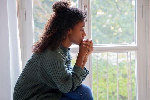 Depression nach Trennung: Traurige junge Frau sitzt vor einem Fenster