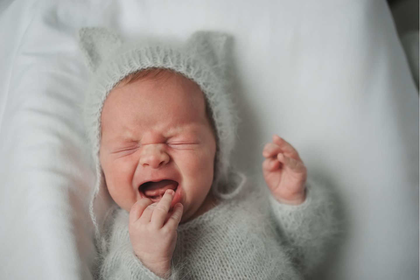 Mamakolumne: Ein schreiendes Baby mit grauer Mütze und Pulli aus Strick